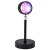 A sunset projection lamp with a black base and stem, and a circular light head emitting pink, purple, and blue light. Podgląd zdjęcia produktu