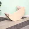 A wooden rocking arch with beige cushions is placed on a striped rug in front of a light green wall. Podgląd zdjęcia produktu