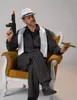 A man dressed in a retro gangster costume sits in a chair, holding a toy gun and a cigar. Produktbild-Vorschau