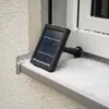 A solar panel device sits on a snow-covered windowsill next to a window. Produktbild-Vorschau