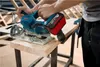 A person is using a cordless circular saw to cut a piece of wood on a workbench. Anteprima dell’immagine prodotto