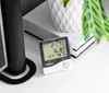 A digital thermometer and hygrometer sits on a white surface next to a black speaker and a white decorative pot with a plant. Anteprima dell’immagine prodotto