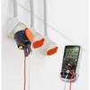A close-up of electrical adapters and a multimeter on a white wall. Produktbild-Vorschau