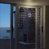 A string of star-shaped LED lights is hung across a glass door, illuminating a brick fireplace and a chair on a balcony. Produktbild-Vorschau