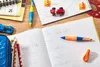 A desk with school supplies, including an open notebook with handwriting, pens, pencils, and small toy cars. Anteprima dell’immagine prodotto