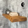 A wooden shelf mounted on a textured gray wall, decorated with books and decorative jars. Produktbild-Vorschau