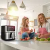 A mother and daughter are in a kitchen, preparing food. The daughter is sitting on the counter next to an air fryer, while the mother is chopping vegetables. Produktbild-Vorschau