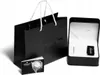 A black shopping bag, an open watch box with a watch inside, and a small booklet are displayed against a white background. Produktbild-Vorschau
