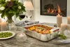 A table setting with a roasting pan, food, wine, and candles, with a fireplace in the background. Produktbild-Vorschau