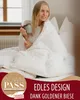 A woman is sitting in bed, wrapped in a white duvet, holding a mug. Produktbild-Vorschau