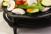 A close-up view of a cast iron grill rack filled with various chopped vegetables, including mushrooms, zucchini, carrots, and bell peppers, placed on a multi-tiered black cast iron stand. Produktbild-Vorschau