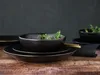 A stack of black plates and bowls with green sprouts in the top bowl, set on a wooden surface with a dark background. Náhľad obrázku produktu