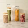Four glass storage jars of different sizes filled with food items, arranged on a countertop against a tiled wall. Produktbild-Vorschau
