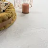 A close-up view of a fluffy white rug with a yellow cushion and a candle in the background. Voir les images du produit