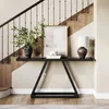 A black console table with a lamp, framed artwork, books, and a vase with greenery, placed in a hallway next to a staircase. Produktbild-Vorschau