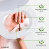 A person's hands are shown applying nail polish under a Lumeno magnifying lamp. The lamp has informational callouts pointing to its features. Produktbild-Vorschau