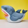 A plush toy shark with its mouth open, revealing a small orange object inside. The background is bright yellow. Podgląd zdjęcia produktu