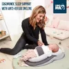 A woman is interacting with a baby lying in an anti-reflux baby nest. Produktbild-Vorschau