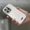 A hand holding a white iPhone 15 Pro with a textured camera lens cover. Produktbild-Vorschau