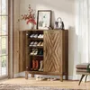 A wooden shoe cabinet with its doors open, displaying shoes on shelves. Decorative items and a handbag are on top of the cabinet. The cabinet is placed in a room with a window and curtains. Náhľad obrázku produktu