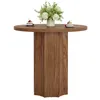 A round wooden dining table with a vase of flowers and two small cakes on top, set against a white background. Produktbild-Vorschau