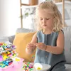 A young girl is sitting on a couch and making a bracelet with beads. Produktbild-Vorschau