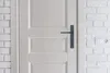 A close-up view of a white door with a dark gray door handle, set against a white brick wall. Anteprima dell’immagine prodotto