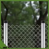 A close-up view of a chain-link fence with two metal posts, set against a blurred background of trees. Produktbild-Vorschau