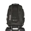 The back of a black Ogio backpack is shown, attached to a rolling suitcase. Produktbild-Vorschau