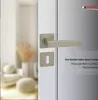 A close-up of a modern door handle and keyhole escutcheon set in a satin nickel finish, with a blurred interior scene in the background and marketing text on the right. Produktbild-Vorschau