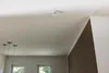 A smoke detector is mounted on a white ceiling in a room with a brown accent wall and pendant lights. Voir les images du produit