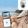 A person relaxing in a hammock on a beach, holding a smartphone that displays a live feed from a security camera. Anteprima dell’immagine prodotto