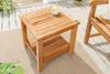 A wooden side table on a patio with a chair and plants. Produktbild-Vorschau