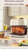 A transparent air fryer with fried chicken inside, placed on a kitchen counter with food and a glass of wine nearby. Produktbild-Vorschau