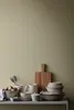 A collection of kitchenware, including bowls, plates, a pitcher, and a cutting board, arranged on a shelf against a light green wall. Produktbild-Vorschau