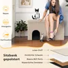 A woman is putting on high heels next to a beige cat house/ottoman with a cat on top. Produktbild-Vorschau