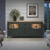 A dark green sideboard with a wood-tone top is shown in a dimly lit room, styled with decorative items and plants. Podgląd zdjęcia produktu