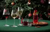 A festive Christmas scene with drinks on a green tablecloth in front of a decorated Christmas tree. Produktbild-Vorschau
