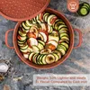 A top-down view of a copper-colored pan filled with a spiral of sliced vegetables, likely ratatouille, with a lid placed nearby. The pan is on a textured gray surface, with some spices scattered around. Produktbild-Vorschau