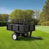 A black utility trailer is parked on a green lawn with trees and a blue sky in the background. Náhľad obrázku produktu