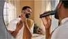 A man is shaving his beard in front of a mirror in a bathroom. Anteprima dell’immagine prodotto