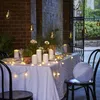 An outdoor table setting at dusk, decorated with string lights and candles. Náhled obrázku produktu