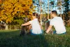 A couple and their dogs sitting on grass in a park during autumn. Produktbild-Vorschau