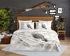 A bedroom scene with a bed dressed in bedding featuring a snowy owl print, decorated with rustic and natural elements. Produktbild-Vorschau