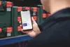 A person is holding a smartphone displaying a map application, with rows of green toolboxes with red latches in the background. Voir les images du produit