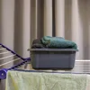 A dark gray plastic basin filled with folded towels sits on a white drying rack. Anteprima dell’immagine prodotto