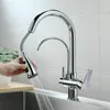 A hand is holding a pull-down faucet sprayer, with water spraying into a sink. The faucet is a modern, chrome-finished kitchen faucet with a separate filtered water spout. Náhled obrázku produktu