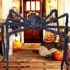 A large, fuzzy black spider decoration is placed on a wooden porch with pumpkins and other Halloween decorations. Produktbild-Vorschau