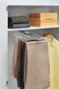 Inside a closet, a multi-tier hanger holds several pairs of pants. On the shelf above, folded sweaters and a wooden box are visible. Produktbild-Vorschau