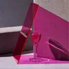 A single glass of pink liquid is placed on a pink surface, with a red translucent acrylic sheet leaning against a pink textured wall. A gray concrete block is in the background. Náhľad obrázku produktu